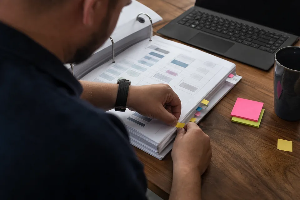 Security lead marking up a printed control mapping binder with colored tabs at a small office table